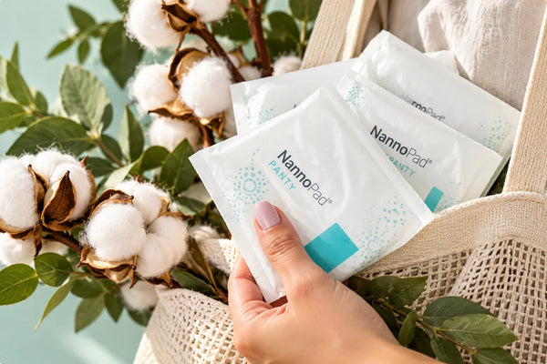 Mano sosteniendo pantiprotectores NannoPad de algodón orgánico junto a flores de algodón